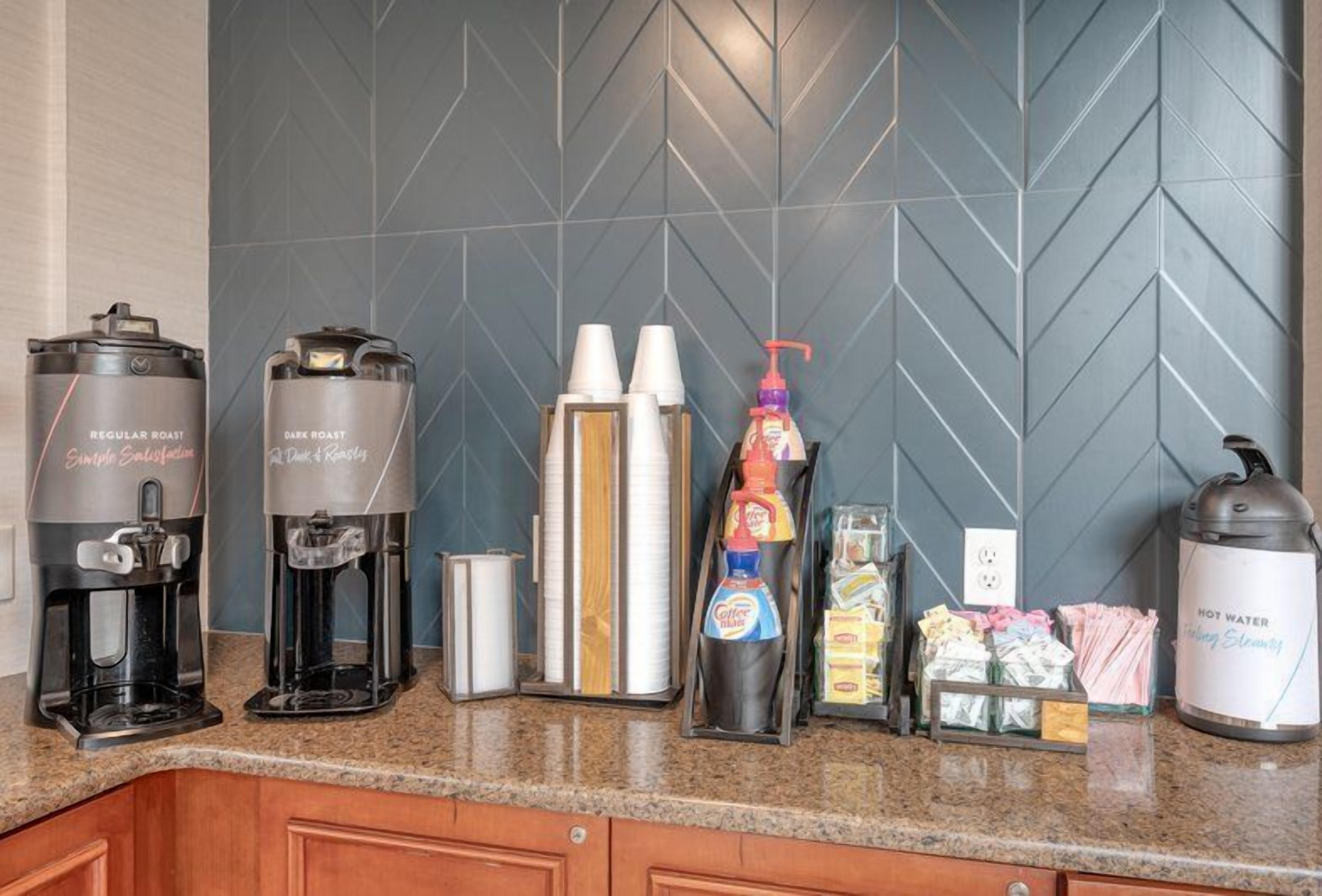 A coffee station with two coffee makers, a bottle of coffee creamer, and a hot water dispenser.