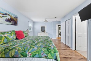 Ein Schlafzimmer mit einem Bett, einem Deckenventilator, einem Gemälde an der Wand und einem zur Tür führenden Flur.
