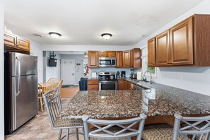 A modern kitchen with granite countertops, stainless steel appliances, wooden cabinets, and a dining area with a table and chairs. -   Adorable Cape May Villas Beach House - Pet Friendly with the Best Sunsets (Lower Township)