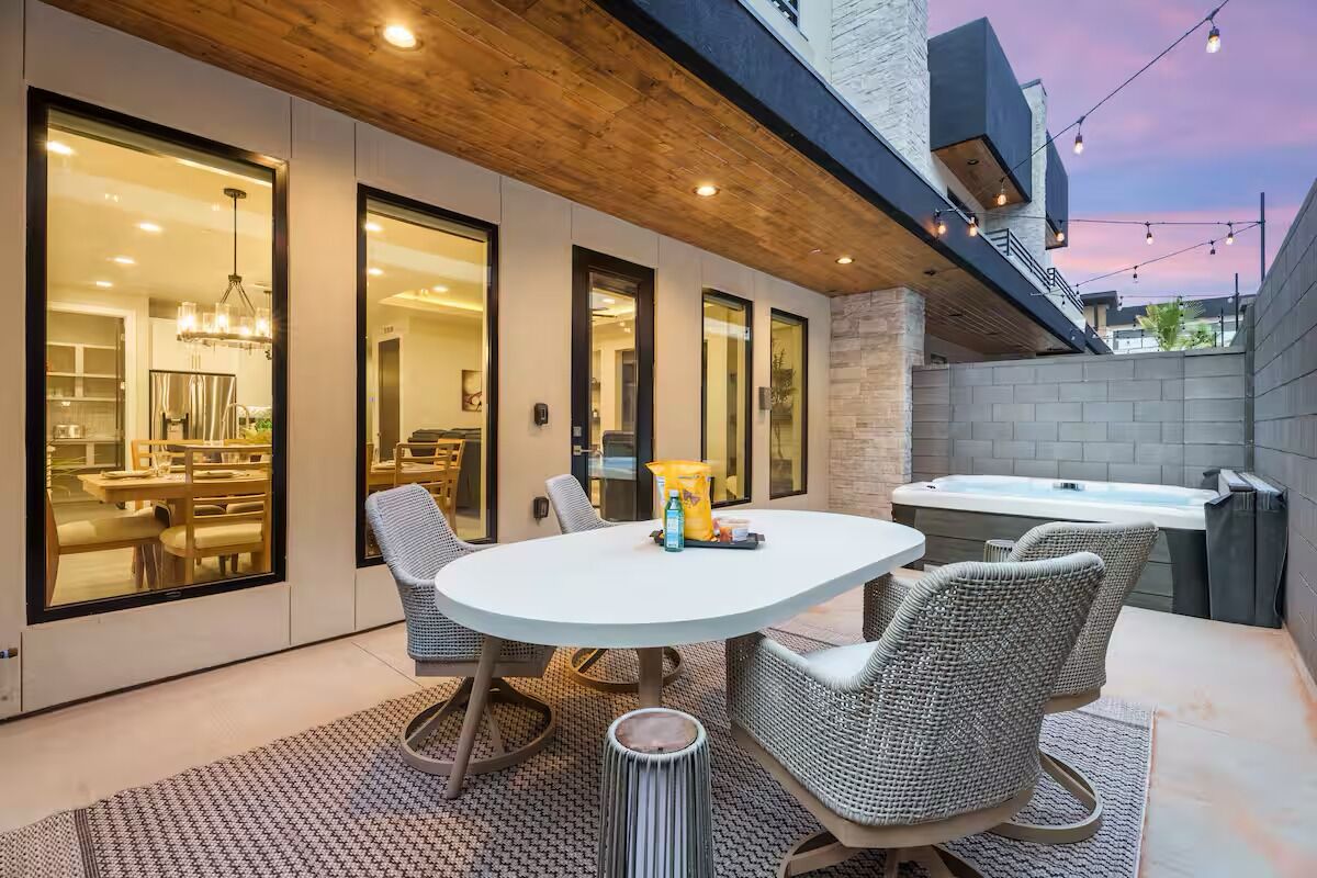 An outdoor patio with a round table and wicker chairs, a hot tub, and a view of the interior dining area.