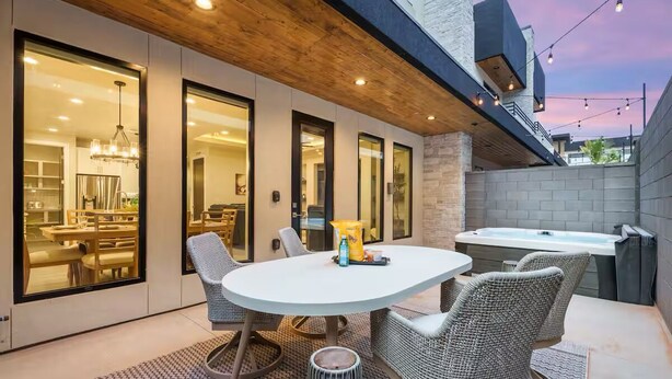 An outdoor patio with a round table and wicker chairs, a hot tub, and a view of the interior dining area. - Zion Vacation - Sleeps 12 - Hot Tub, Golf, Waterpark (Hurricane)
