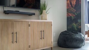 A modern living room with a wooden cabinet, a flat-screen TV, a potted plant, and a bean bag. - Zion Vacation - Sleeps 12 - Hot Tub, Golf, Waterpark (Hurricane)