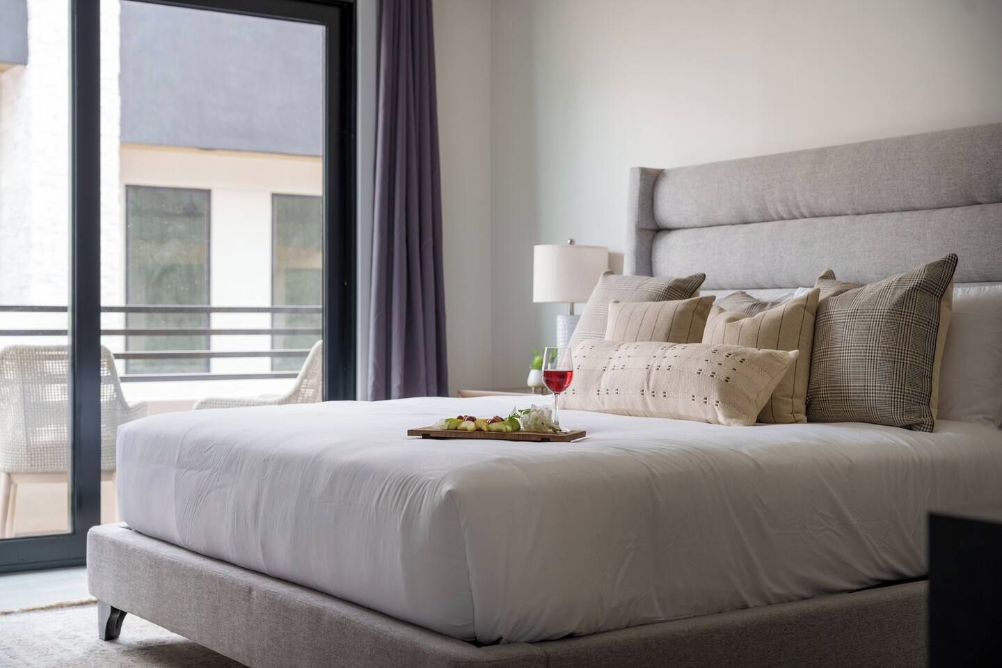 Quarto de hotel com cama grande, varanda com cadeira e vista para edifícios.