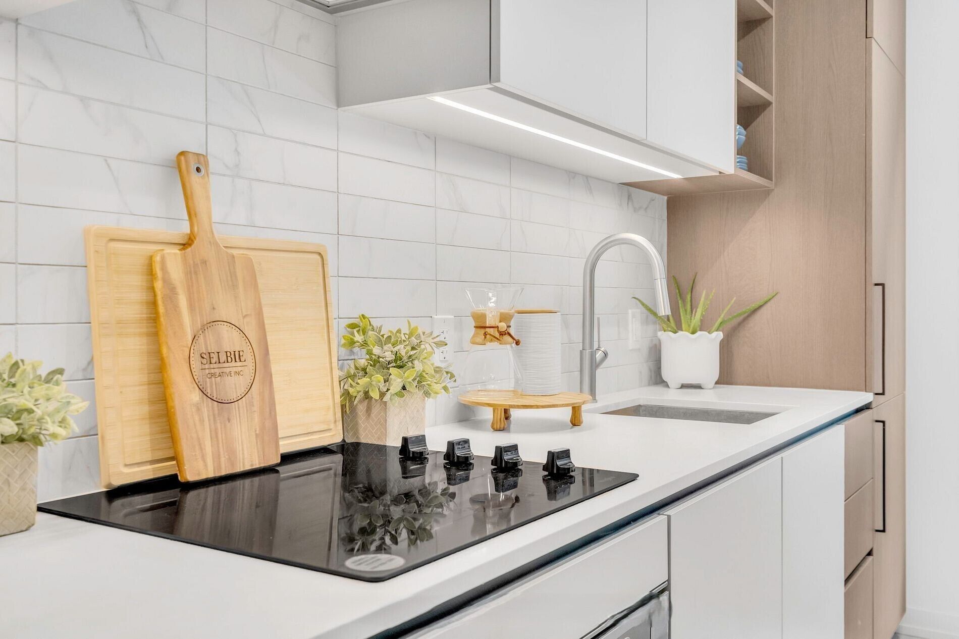 A modern kitchen with a black induction cooktop, wooden cutting board, and white cabinets.