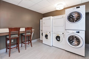 Une buanderie équipée de machines à laver et de sèche-linge superposés, de deux chaises en bois et d’un luminaire au plafond.