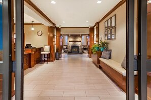 Eine Hotellobby mit Kamin, Sitzgruppe, Rezeption und einer Wanduhr.