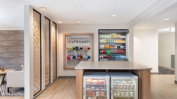 Uma cozinha compacta moderna, com área refrigerada, um armário identificado como 'CANDLEWOOD CUPBOARD' e uma parede com padrão geométrico.
