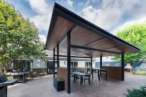 A covered outdoor patio with a dining area, a barbecue grill, and a stone planter.