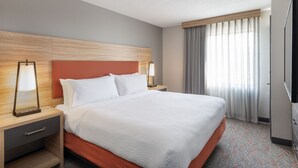 A hotel room with a large bed, wooden headboard, two bedside lamps, a TV, and a window with curtains.