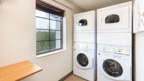A laundry room with two stacked washing machines and a window with blinds. - Accessible Suite with Soaking Tub & Full Kitchen (Eagan)