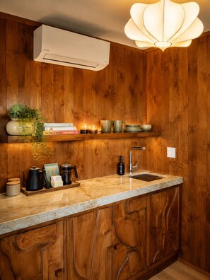 Una cocina con paneles de madera, encimera de mármol, lavaplatos, cafetera y una lámpara colgante.