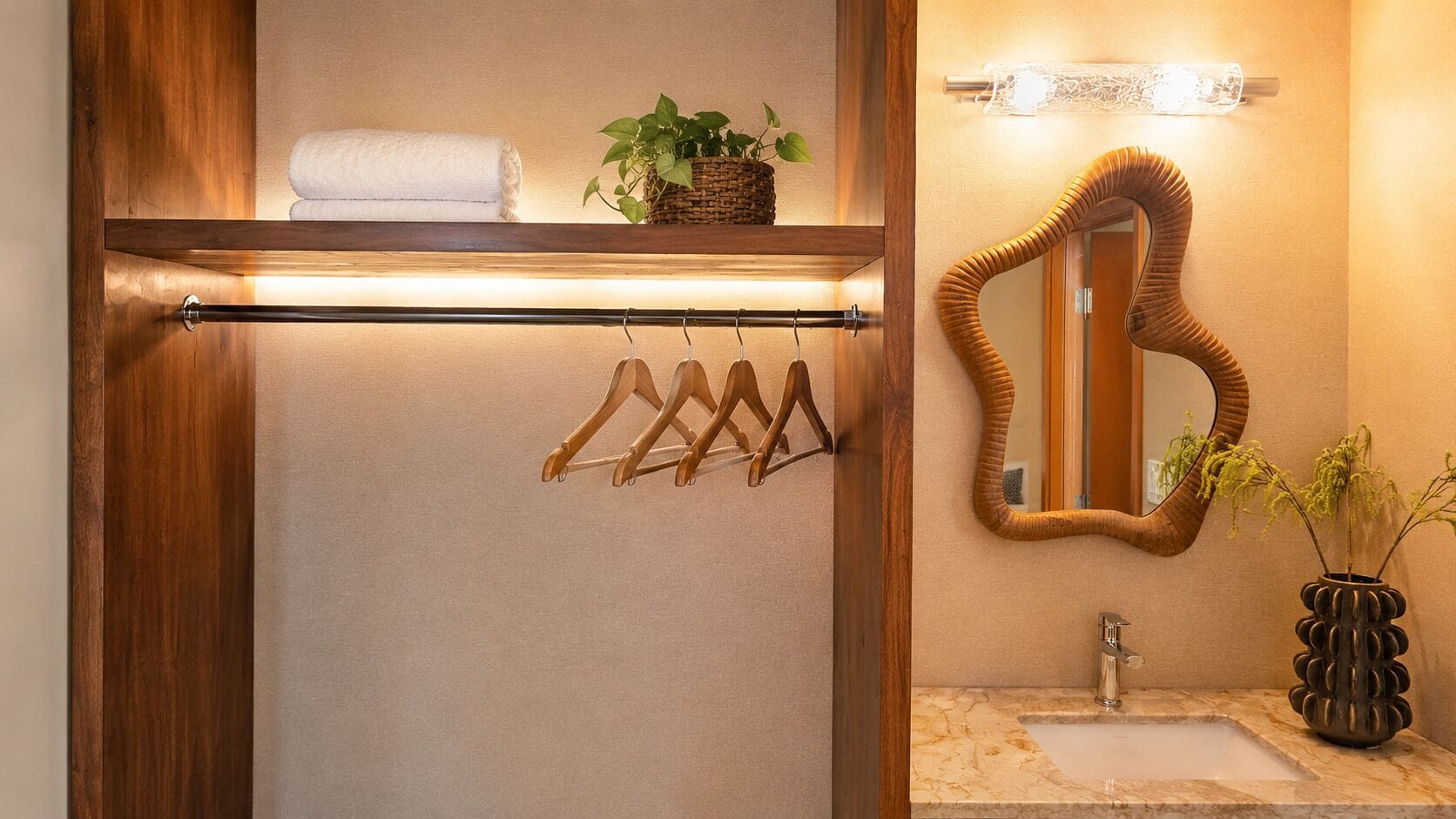 A bathroom with a wooden towel rack, a hanging towel, a mirror with a curved frame, and a plant in a decorative vase.