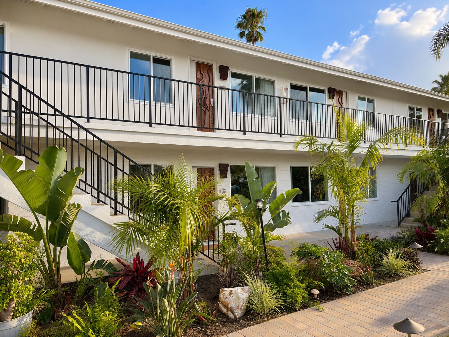 A two-story building with a balcony, surrounded by tropical plants and a paved walkway.
