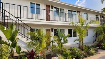 A two-story building with a balcony, surrounded by tropical plants and a paved walkway.