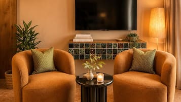 A living room with two armchairs, a coffee table, a flat-screen TV, a decorative lamp, and a wall-mounted air conditioner.