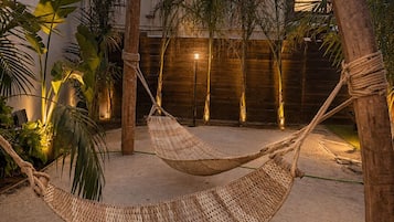 A hammock in a sandy outdoor area with a wooden fence and palm trees.