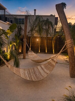 A hammock in a sandy outdoor area with a wooden fence and palm trees.