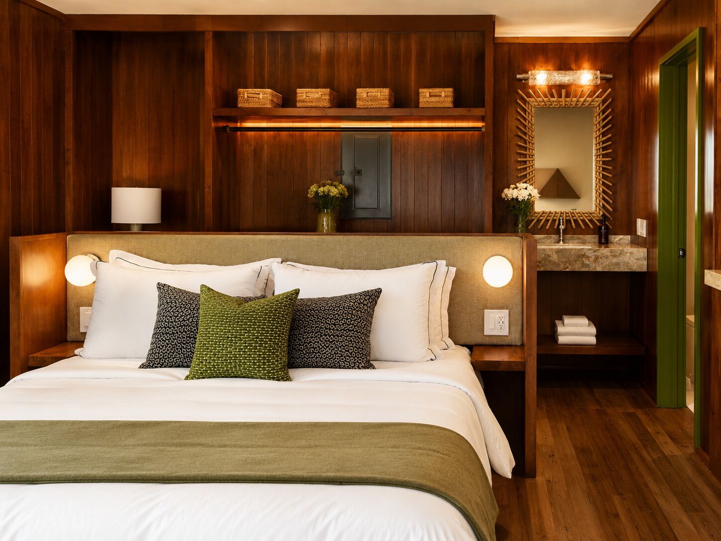 Habitación de hotel con una cama grande, lámparas de noche, un cabecero de madera, un tocador con espejo y una puerta verde.
