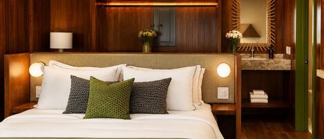 Habitación de hotel con una cama grande, lámparas de noche, un cabecero de madera, un tocador con espejo y una puerta verde.