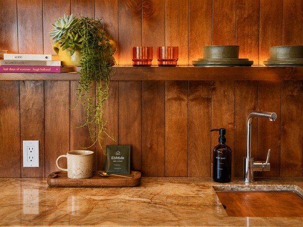 Una cocina de madera con cafetera, botella de detergente para platos y una planta en maceta.