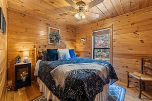 Un cuarto acogedor de madera con una cama, una mesita de noche, una silla y una ventana con vistas a árboles.