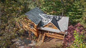 Eine Blockhütte mit einem steilen Walmdach, umgeben von dichtem Wald.