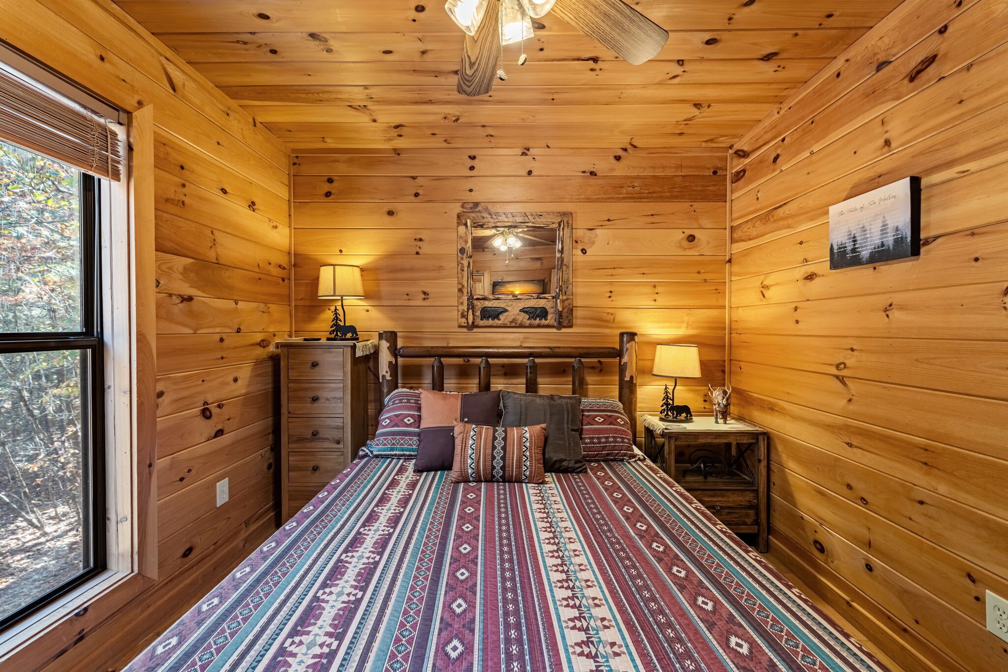 A wooden cabin bedroom with a bed, two bedside tables, a dresser, and a window.