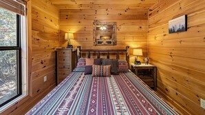 A wooden cabin bedroom with a bed, two bedside tables, a dresser, and a window. - Dogwood Lodge - Hot Tub, Near Kerith House Winery (Morganton)
