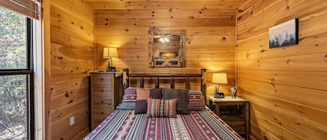 A wooden cabin bedroom with a bed, two bedside tables, a dresser, and a window.