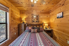 Ein Schlafzimmer einer Holzhütte mit einem Bett, zwei Nachttischen, einer Kommode und einem Fenster.