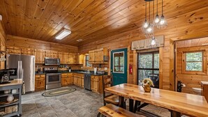 A wooden cabin kitchen with a dining table, benches, a refrigerator, stove, microwave, and a window with a view of trees. - Dogwood Lodge - Hot Tub, Near Kerith House Winery (Morganton)