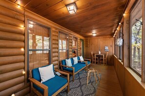 Interior de una cabaña de troncos con sofá, una mesa de comedor y vista al bosque.