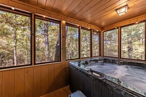Eine Holzhütte mit Whirlpool und großen Fenstern mit Blick auf einen Wald.