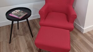 A red armchair with a matching ottoman, a small black table with books, and a wooden floor. - Charming 1-bedroom bungalow with AC in Oak Bluffs (Oak Bluffs)