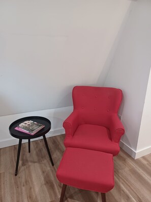 A red armchair with a matching ottoman, a small black table with books, and a wooden floor. - Charming 1-bedroom bungalow with AC in Oak Bluffs (Oak Bluffs)