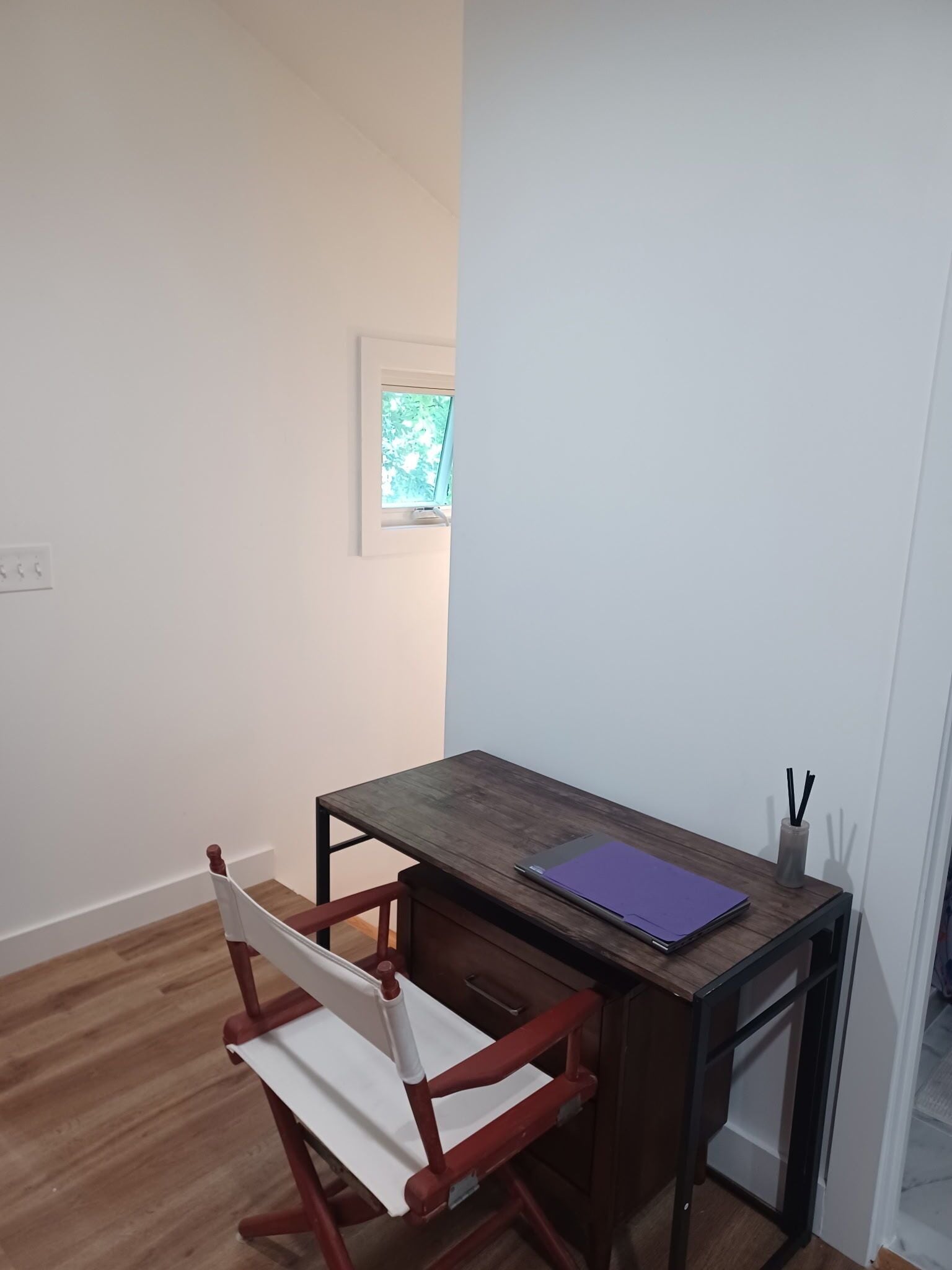 Habitació petita i ben ordenada amb escriptori de fusta, una cadira i un quadre al mur.