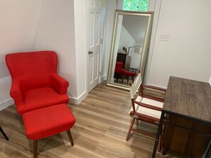 Quarto com uma poltrona vermelha, uma mesa de madeira e um espelho refletindo uma cadeira vermelha e um abajur.