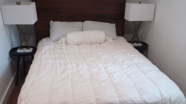 A neatly made bed with a white quilt, two bedside tables with lamps, and a wooden headboard. - Charming 1-bedroom bungalow with AC in Oak Bluffs (Oak Bluffs)