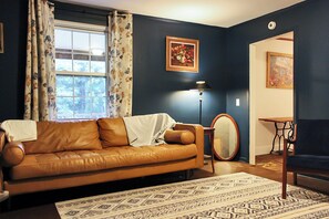 Ein Wohnzimmer mit braunem Ledersofa, einem gemusterten Teppich, einer Stehlampe und einem Bild an der Wand.
