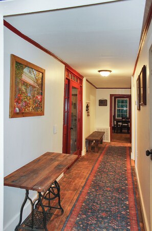 Un couloir avec un banc en bois, une porte rouge et un tapis à motifs.