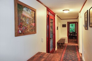 A hallway with a wooden bench, a door with a red frame, and a framed picture on the wall.