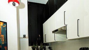 A modern kitchen with black and white cabinetry, a black countertop, a microwave, a kettle, and a small dining area with a table and chairs. - LH51 Urban Suite – Design & Luxury in the Historic Center of Naples (Napoli)