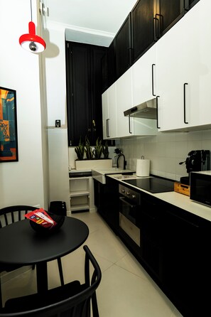 A modern kitchen with black and white cabinetry, a black countertop, a microwave, a kettle, and a small dining area with a table and chairs. - LH51 Urban Suite – Design & Luxury in the Historic Center of Naples (Napoli)