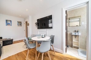 Ein modernes Wohnzimmer mit einem runden Esstisch, grauen Stühlen, einem grauen Sofa und einem an der Wand befestigten Flachbildfernseher.