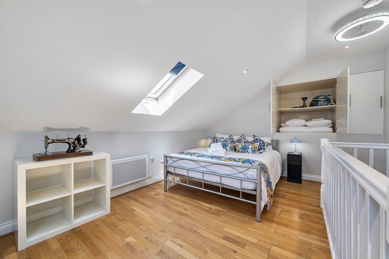 Ein Schlafzimmer mit Dachfenster, einem Bett mit blumigem Bettbezug, einer Nähmaschine auf einem Regal und einem weißen Kleiderschrank.