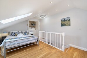 Ein Schlafzimmer mit Dachfenster, einem Bett mit gemustertem Überwurf, einem weißen Geländer und einem Bild an der Wand.