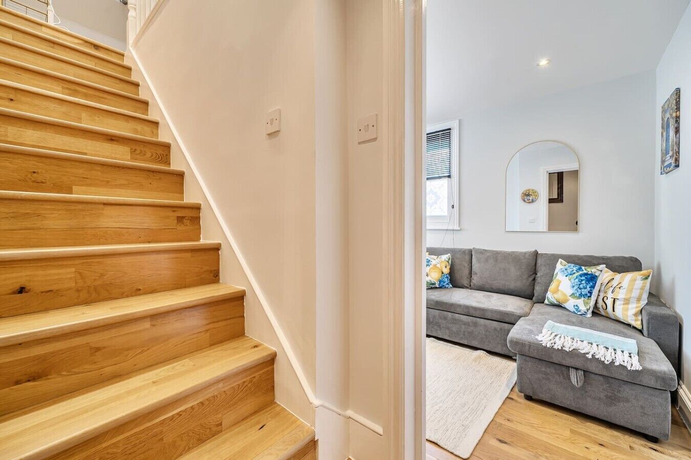 Un escalier en bois mène à un espace de vie agrémenté d’un canapé gris et de coussins décoratifs.