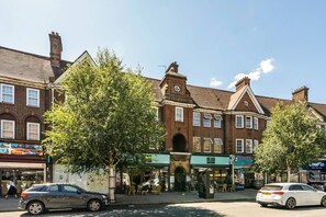 Eine Straßenszene mit einer Reihe aus Ziegelgebäuden, einem Café mit Außenbestuhlung und parkenden Autos.