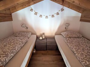 A small, cozy attic bedroom with two beds, a wooden ceiling, and a string of decorative lights. - Sper Prada by Interhome (Churwalden)