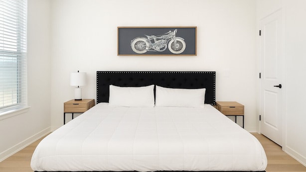 Quarto com uma cama grande, cabeceira, duas mesas de cabeceira, um criado-mudo, janela com persianas e um quadro emoldurado na parede.
